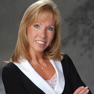 Professional woman with blonde hair wearing a black blazer and white blouse, smiling against a grey background