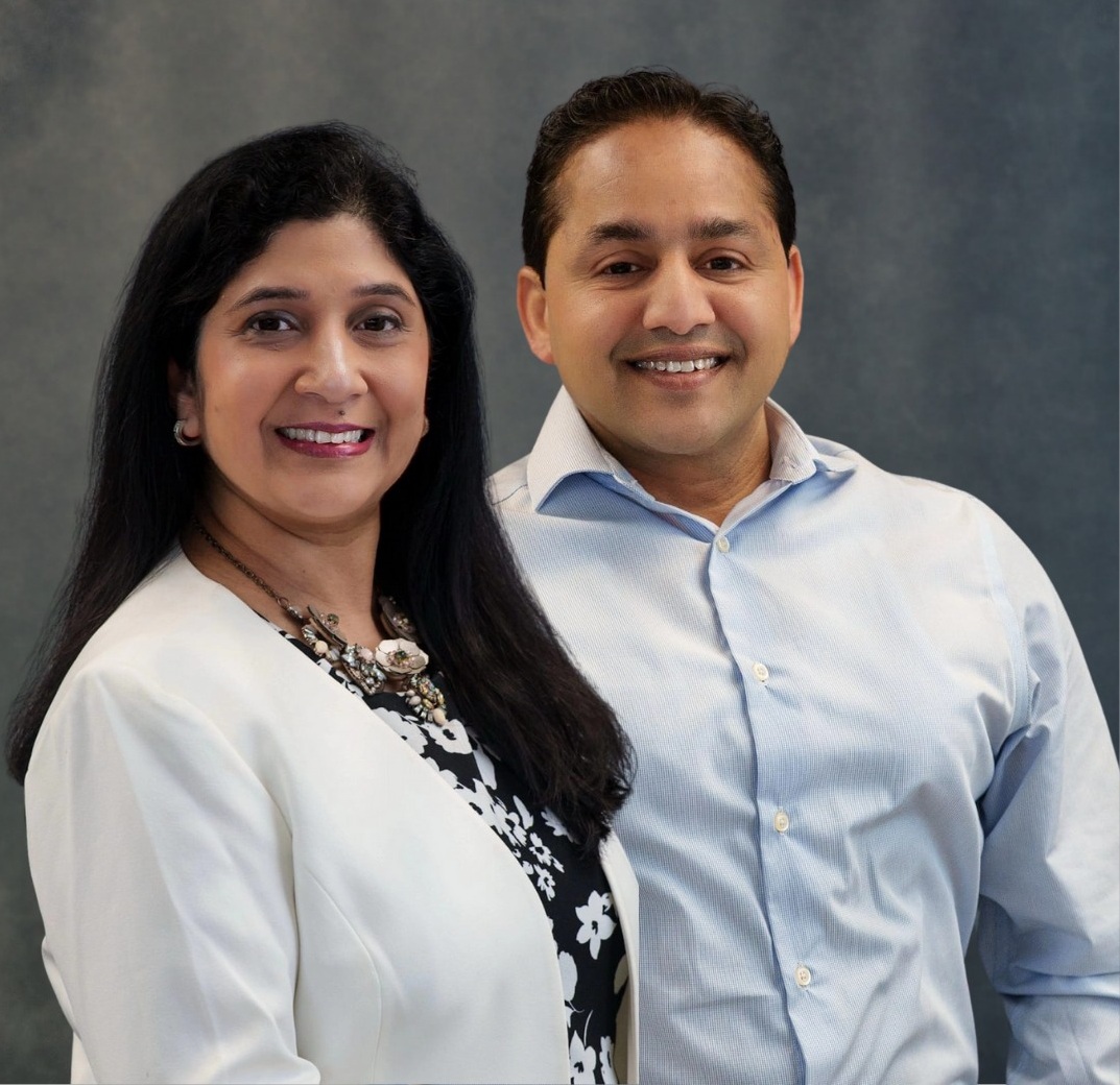 Professional headshot of a businessman in a dark suit, maroon shirt, and striped tie, smiling against a blue background