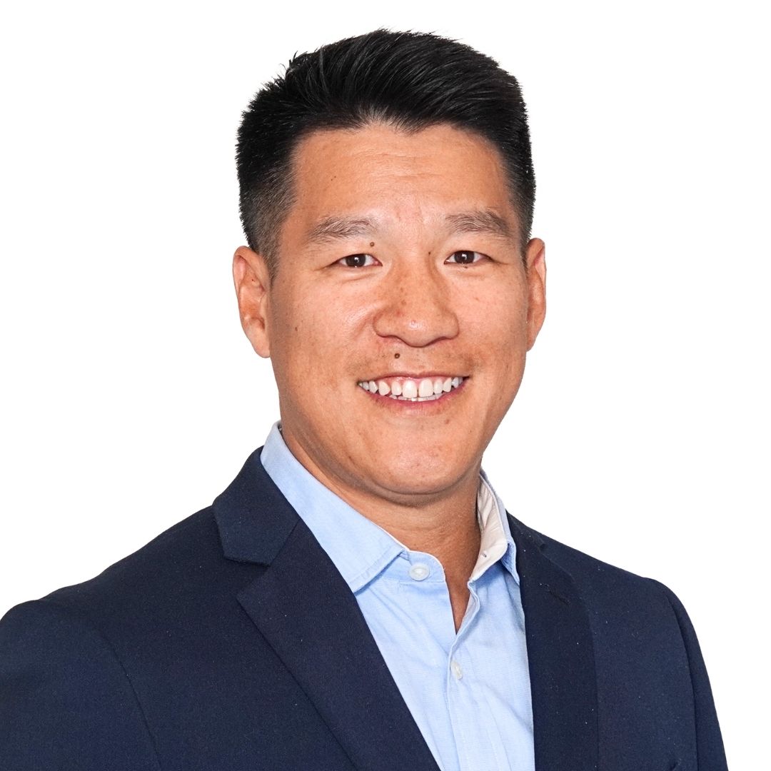 Smiling Asian man in business suit with shaved head, wearing white shirt and dark blazer, professional portrait against neutral background