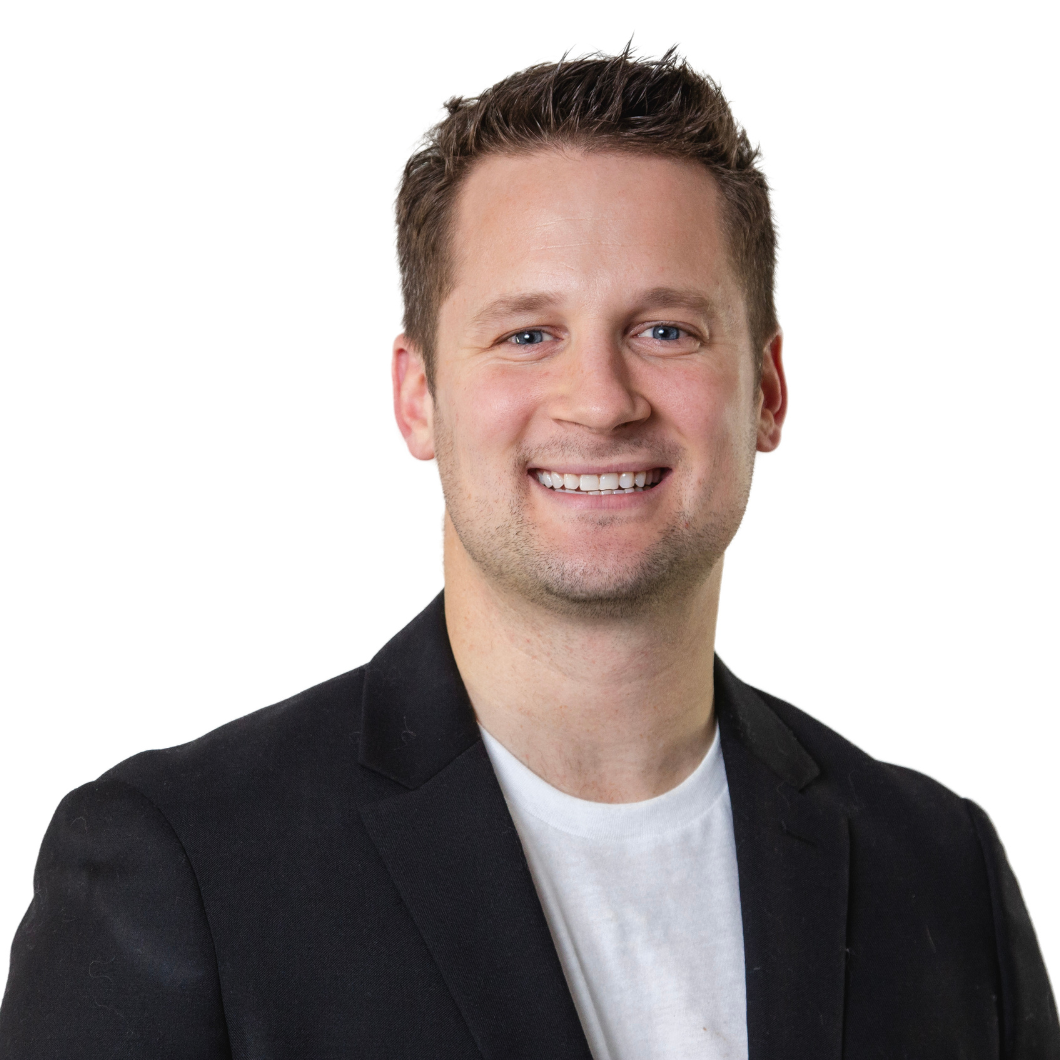 Smiling young man in a black blazer and white t-shirt, professional portrait with a plain white background.
