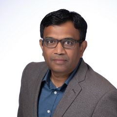 Professional portrait of a man in a grey suit and glasses against a white background