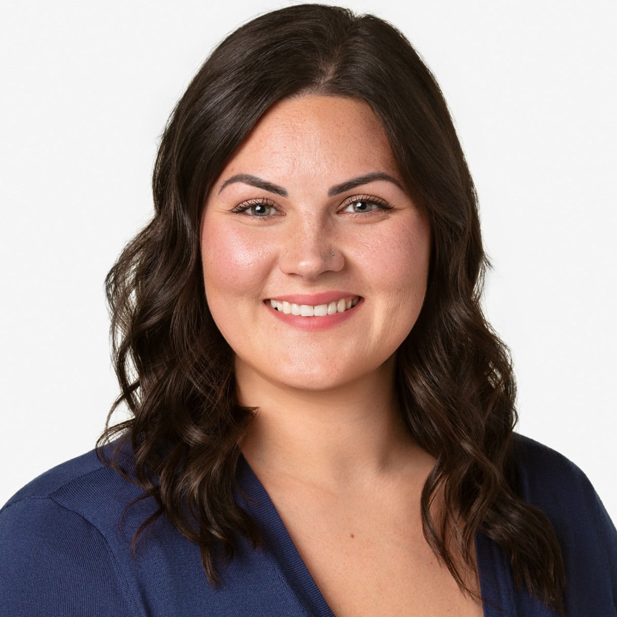 Portrait of a smiling woman with dark wavy hair, wearing a navy blue top, against a plain white background.