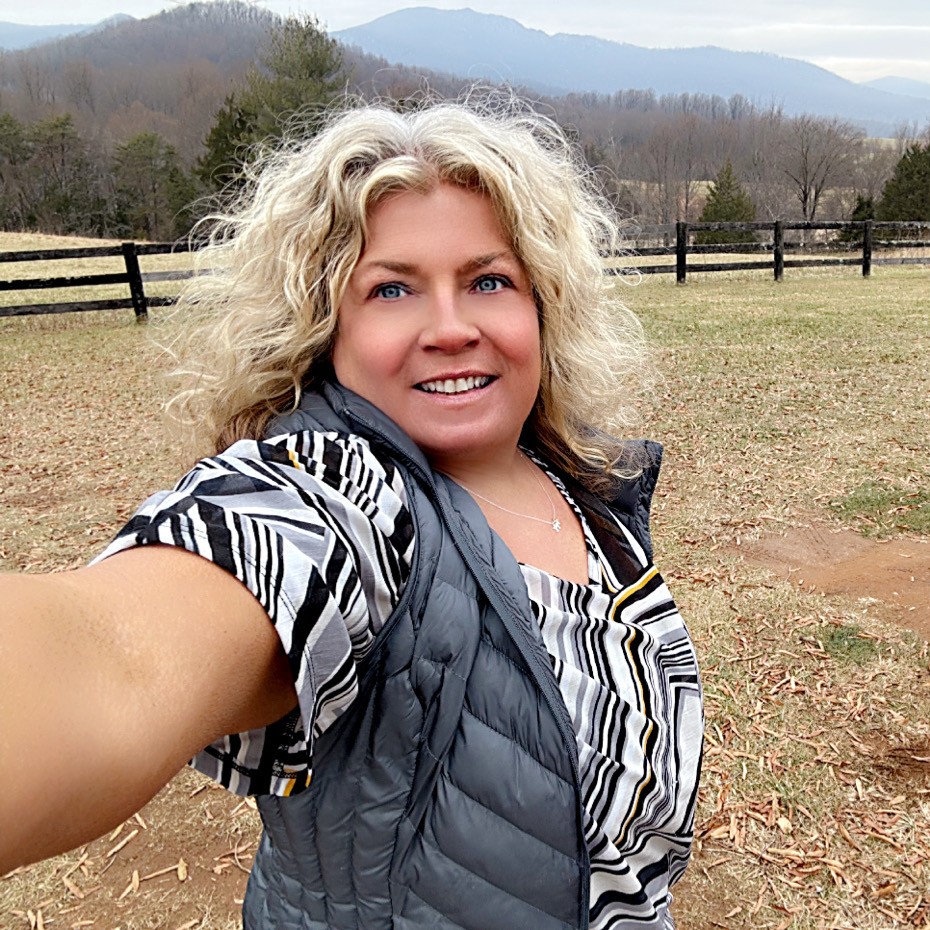 Smiling elderly man with gray hair, glasses, pink shirt, and maroon sweater in a modern office setting.